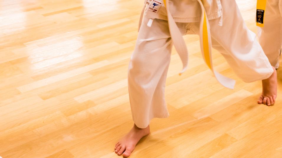 Trainer überreicht einem Mädchen in Karate-Gi mit gelbem Gürtel zwei blaue Urkunden während des Trainings.